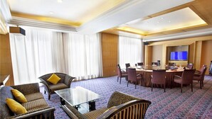 Una habitación de hotel con una amplia zona de estar, una mesa de conferencias y un televisor.