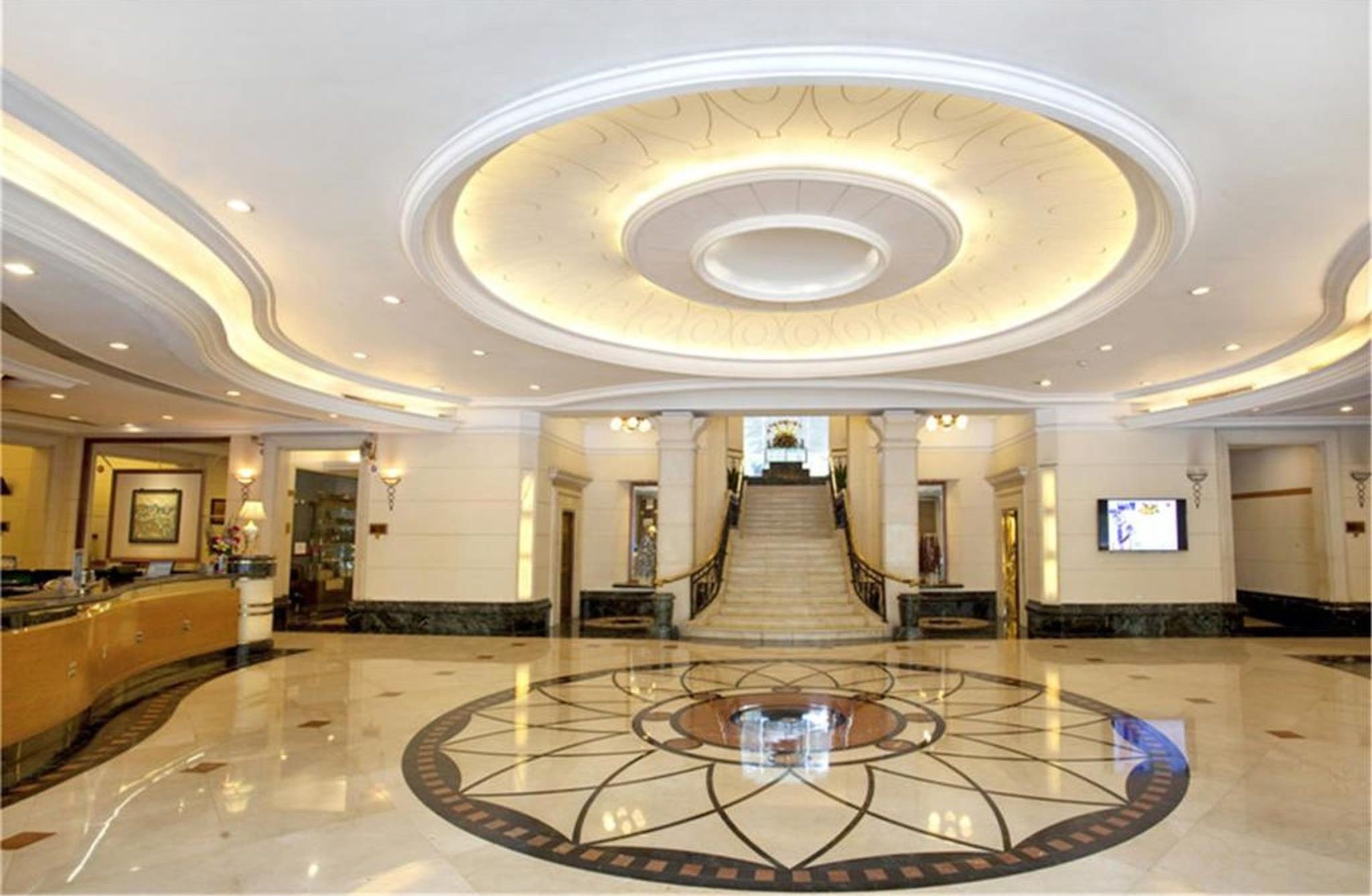 A spacious lobby with a grand staircase, marble flooring, and a central circular design.
