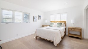 Un dormitorio con una cama, dos mesitas de noche y dos ventanas con persianas.