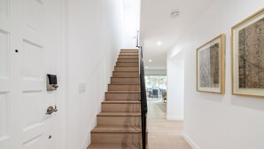 Una escalera de madera con barandilla negra que conduce a una habitación con paredes blancas y una puerta.