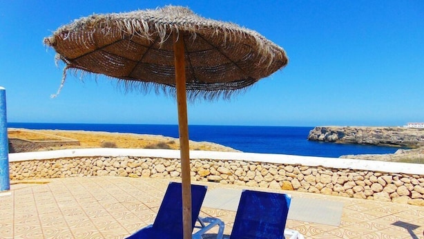 A beachside lounge with two blue lounge chairs and a straw umbrella. - Bluesea Cabo de Banos (Ciutadella de Menorca)