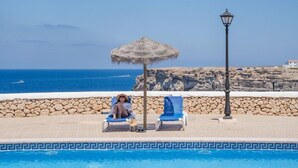 A pool area with a stone wall, a thatched umbrella, and a lamp post. - Bluesea Cabo de Banos (Ciutadella de Menorca)
