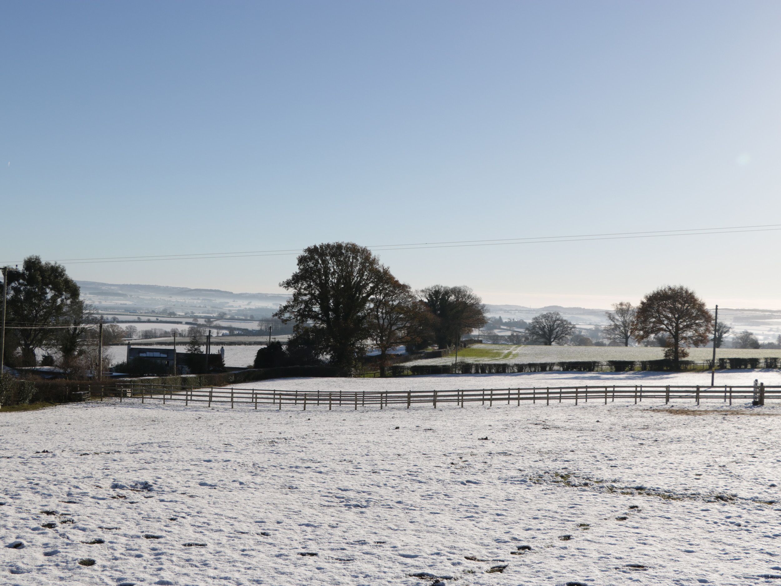 A snow-covered field with a wooden fence and trees in the background.