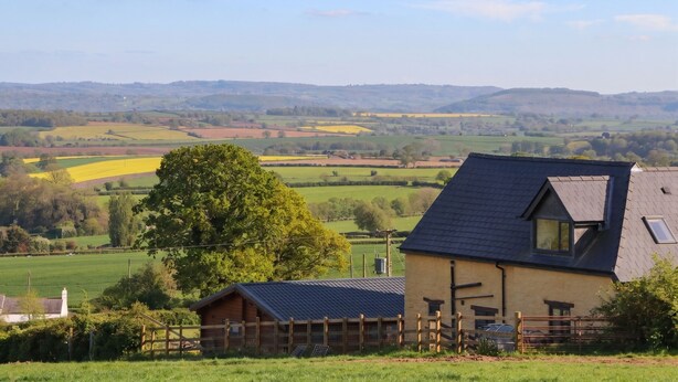 A rural landscape with a house featuring a dark roof and a wooden fence. - Palace Studio (Hereford)
