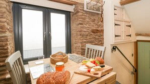 A cozy dining area with a stone wall, wooden table, and chairs. A window with a view is visible, and a small staircase leads to an upper level. - Palace Studio (Hereford)