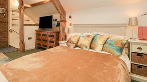 A bedroom with a large bed, wooden beams, a TV, a dresser, and a lamp. - Palace Studio (Hereford)