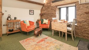 A cozy living room with a stone wall, a wooden table, two orange chairs, a small bull sculpture, and a colorful rug. - Palace Studio (Hereford)