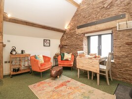 Un salón acogedor con una pared de piedra, una mesa de madera, dos sillones naranja, una pequeña escultura de toro y una alfombra colorida.