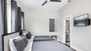 A bedroom with two beds, a ceiling fan, a painting, and a view into the bathroom. - Nashville Luxe Retreat • Rooftop & Hot Tub (Nashville)