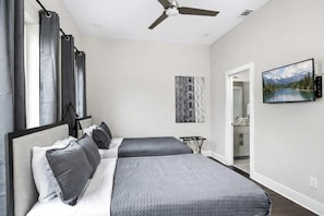 A bedroom with two beds, a ceiling fan, a painting, and a view into the bathroom. - Nashville Luxe Retreat • Rooftop & Hot Tub (Nashville)