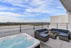 A rooftop terrace with a hot tub, outdoor seating, and a city view.