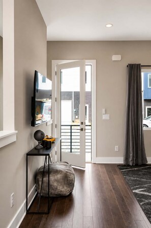 A modern interior with a flat-screen TV, a bench, and a door leading outside. - Nashville Luxe Retreat • Rooftop & Hot Tub (Nashville)