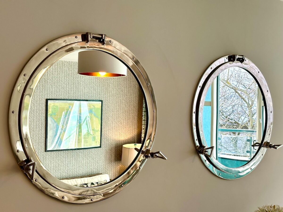 Deux fenêtres circulaires dotées de montures métalliques, l’une présentant une carte et l’autre offrant une vue sur des arbres.