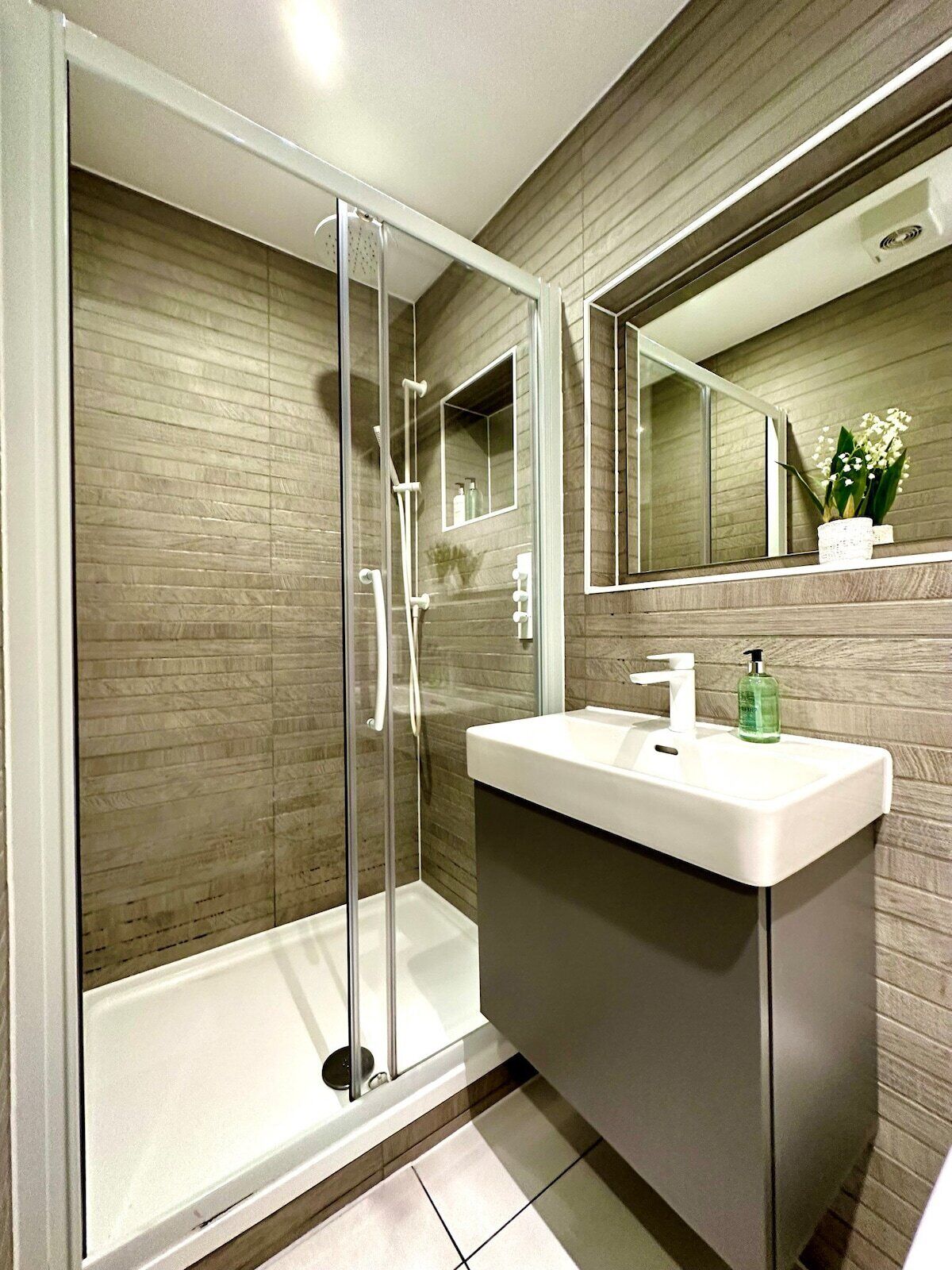 A modern bathroom with a glass-enclosed shower, a white sink, and a mirror above it.