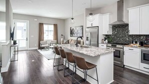Cozinha moderna com ilha central, banquetas, eletrodomésticos de aço inoxidável e painel de azulejos em padrão herringbone.