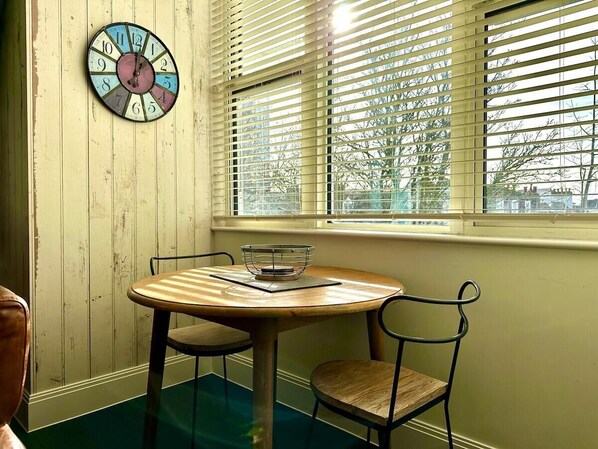 A room with a round wooden table, two chairs, a wall clock, and a window with blinds. - Designer Apartment inc. Free Parking & FAST WiFi (Poole)