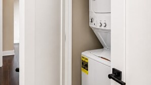 A laundry room with a stacked washer and dryer, a door, and a tiled floor. - Music City Luxe Stay • Rooftop & Hot Tub (Nashville)