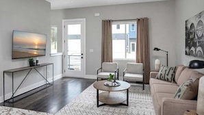 A modern living room with a flat-screen TV, two armchairs, a sofa, a coffee table, and a large window with curtains. - Music City Luxe Stay • Rooftop & Hot Tub (Nashville)