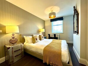 A neatly arranged bedroom with a bed, bedside lamps, a suitcase, and a window.