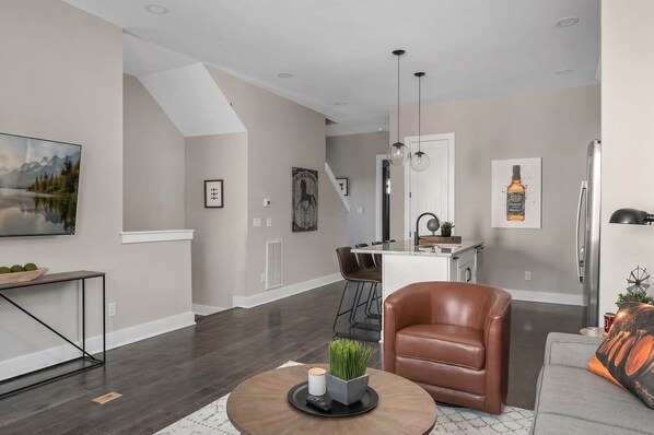 A modern kitchen with a central island, a dining area with a brown leather chair, and a living room with a brown leather sofa.