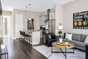 A modern kitchen with stainless steel appliances, a dining area with a bar stool, and a living room with a sofa and coffee table. - Two Luxury Homes • Side-by-Side • Sleeps 24 (Nashville)
