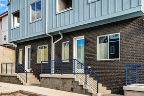A multi-story residential building with a brick facade, a blue exterior, and a set of stairs with blue railings.