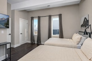 A bedroom with two beds, a desk, a window with curtains, and a painting on the wall.