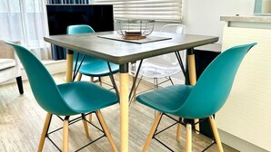 Un comedor moderno con una mesa y cuatro sillas color esmeralda, un televisor en la pared y una ventana con persianas.