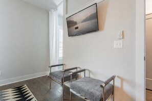 A room with a large window, a flat-screen TV mounted on the wall, and two grey upholstered chairs with metal legs. - 2 New Nashville Homes • Near Vandy & 3 Min to Bars (Nashville)
