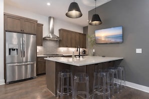 Una cocina moderna con electrodomésticos de acero inoxidable, una isla central con taburetes de bar y un televisor montado.