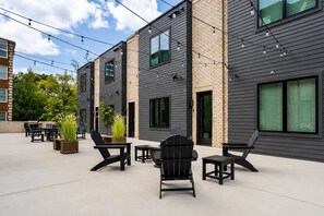 A modern outdoor seating area with chairs and tables, surrounded by a building with large windows and a brick facade.