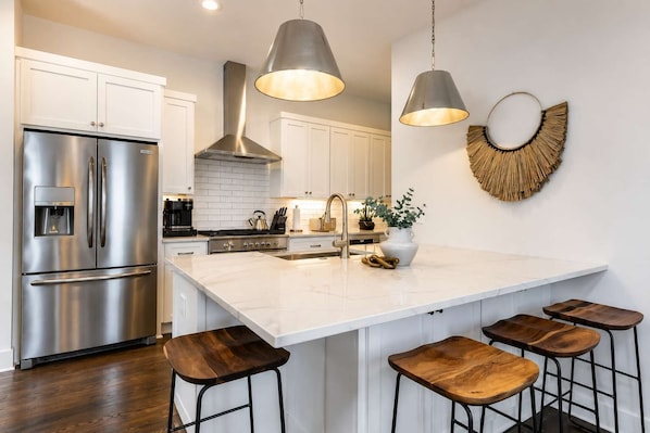 A modern kitchen with stainless steel appliances, a white marble island, and wooden bar stools.