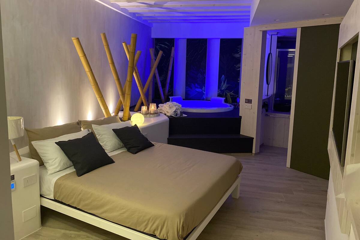 Un dormitorio moderno con cama, mesitas de noche, sillón de masaje e hidromasaje.