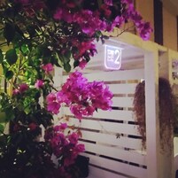 Una estructura blanca con un letrero de neón que dice "HOME 2" y flores rosas en primer plano.