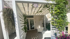 A covered outdoor area with a white pergola, a hanging flower basket, and a potted plant with pink flowers. - Home3 bed (Bisceglie)