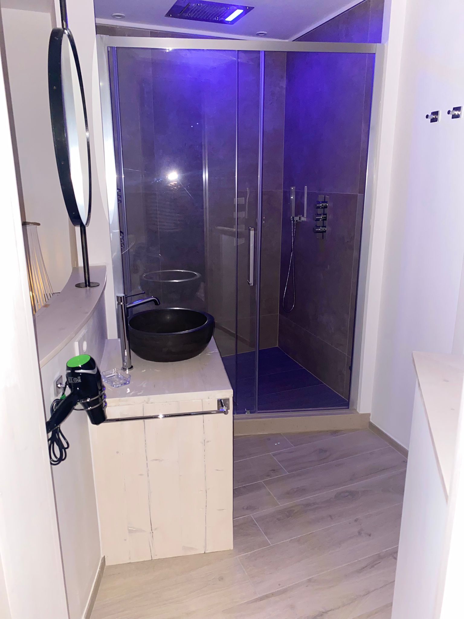 A modern bathroom with a glass shower enclosure, a sink with a black basin, and a mirror on the wall.
