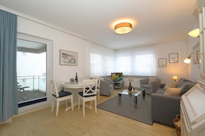 Una sala moderna con comedor, un conjunto de sofás, televisor y balcón con vistas.