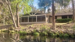 A house with a covered patio area, surrounded by trees and a body of water. - Oak Rock Ranch - Riverfront - Scenic Old Florida (Inglis)