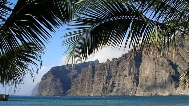 A beach with people swimming and walking along the shore, palm trees, and a large cliff in the background. - Relax Oasis of the Sea, Santiago del Teide (Puerto Santiago)
