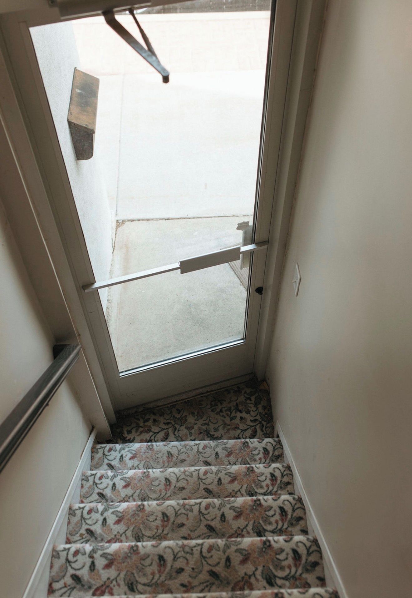 Una escalera con alfombra estampada que lleva a una puerta con picaporte metálico.