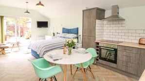 Et moderne soveværelse med en stor seng, et lille spisebord med stole, et tekøkken med komfur og skabe, samt et TV ophængt på væggen.