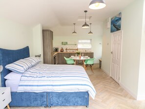 A bedroom with a large bed, a small kitchenette, and a dining area with chairs. - Byghan Thornton (Redruth)