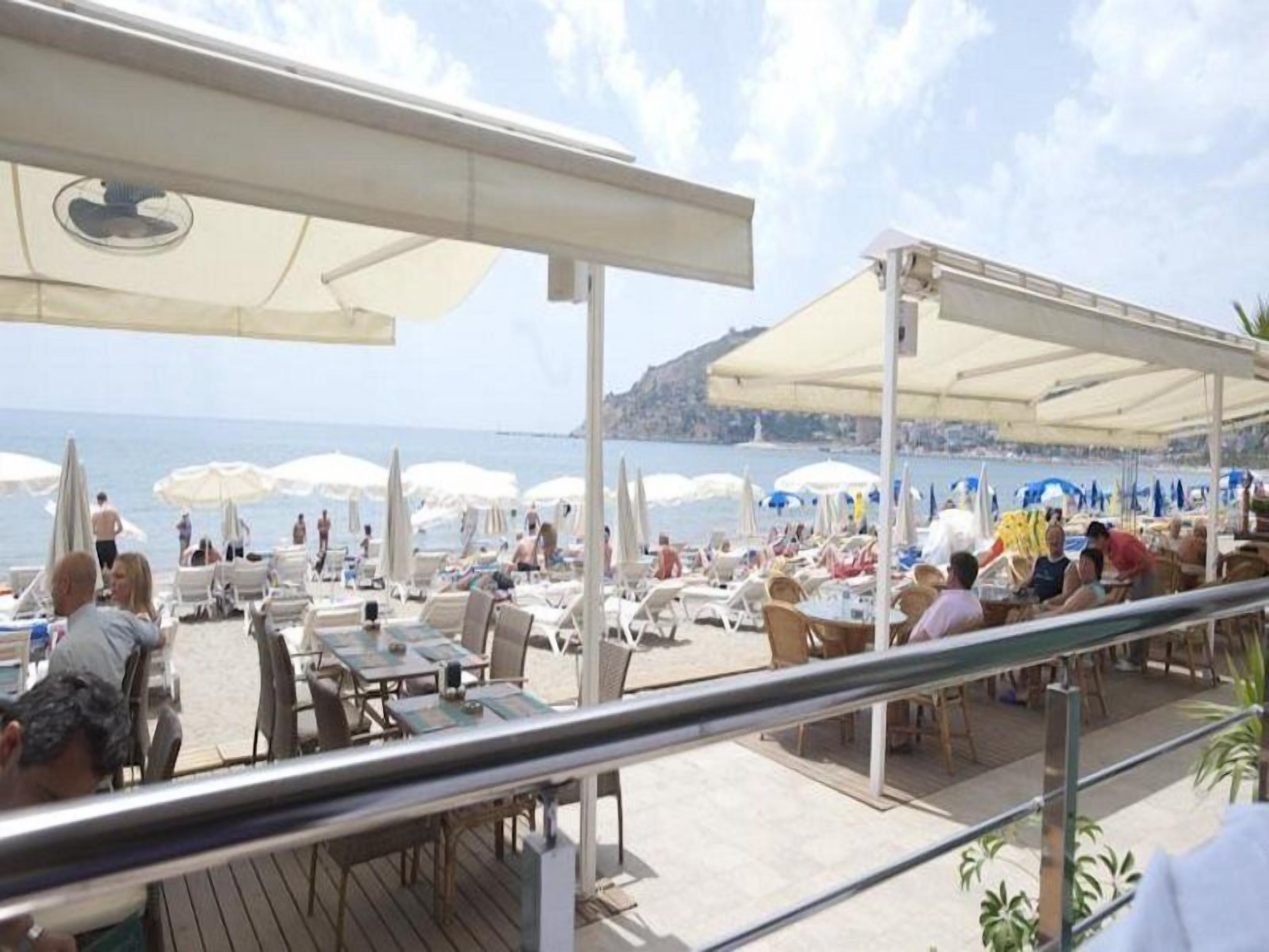 A beachside restaurant with outdoor seating, umbrellas, and a view of the sea.