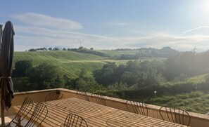 A terrace with a table and chairs, overlooking a green landscape with hills and trees. - Vineyard Farmhouse in Massignano - just minutes from the beach (Massignano)