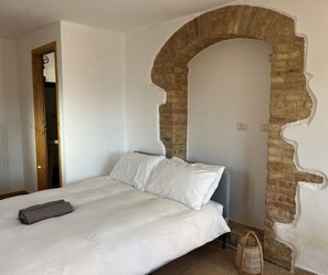 A bedroom with a bed, a wooden door, and a brick archway. - Vineyard Farmhouse in Massignano - just minutes from the beach (Massignano)