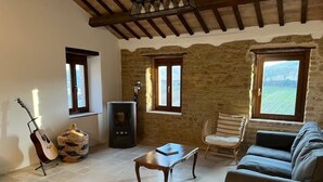 Ein gemütliches Wohnzimmer mit Steinwand, Kamin, einer Gitarre, einem gewebten Korb und Blick ins Freie durch ein Fenster.