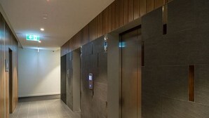 Un espace ascenseur moderne, doté d’un panneau de commande fixé au mur et d’un panneau de signalisation indiquant clairement la sortie de secours.