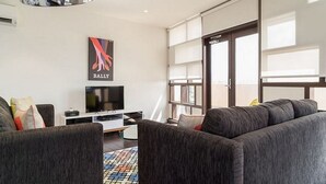 Un salon moderne avec un grand canapé gris, un téléviseur à écran plat et un tapis coloré.