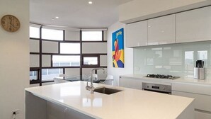 Une cuisine moderne dotée d’un îlot central, d’une grande fenêtre et d’un tableau abstrait aux couleurs vives accroché au mur.