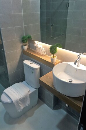 A modern bathroom with a toilet, sink, and shower. There are potted plants on the counter and toiletries on the shelf.